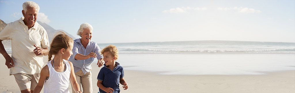 Großeltern laufen fröhlich mit ihren Enkelkindern am Strand